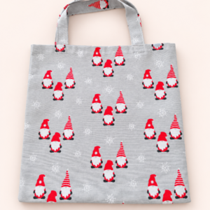 Graue Stofftasche mit zwei Henkeln, Weihnachtswichteln mit roten Mützen und weißen Schneeflocken vor hellem Hintergrund.