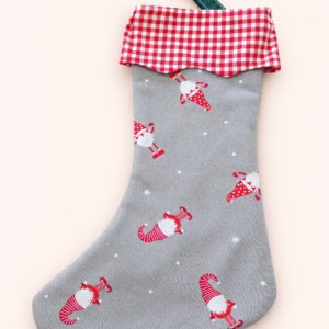 Grauer Weihnachtsstrumpf mit roten Wichtelmotiven, rot-weiß kariertem Bund und grüner Aufhängeschlaufe vor hellem Hintergrund.
