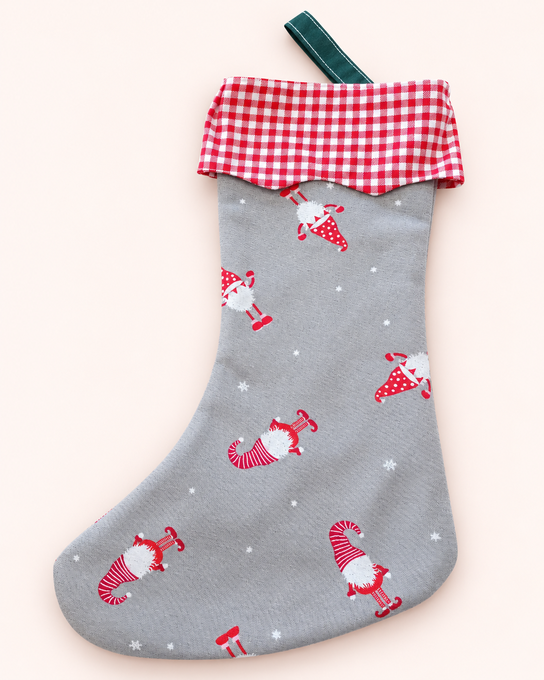 Grauer Weihnachtsstrumpf mit roten Wichtelmotiven, rot-weiß kariertem Bund und grüner Aufhängeschlaufe vor hellem Hintergrund.