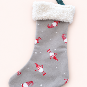 Grauer Weihnachtsstrumpf mit roten Wichtelmotiven, weißem Plüschbund und grüner Aufhängeschlaufe vor hellem Hintergrund.